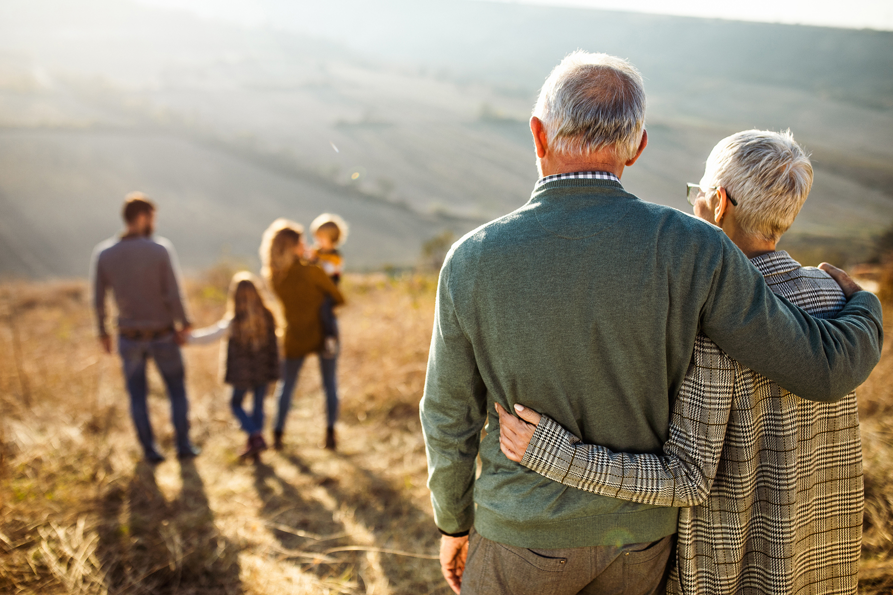 Older couple embracing while looking at their family, representing planning for funeral and final expenses with a cost estimation calculator.