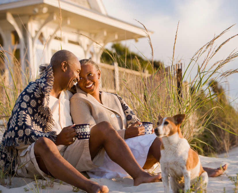 retired couple sitting on the beach with their dog​