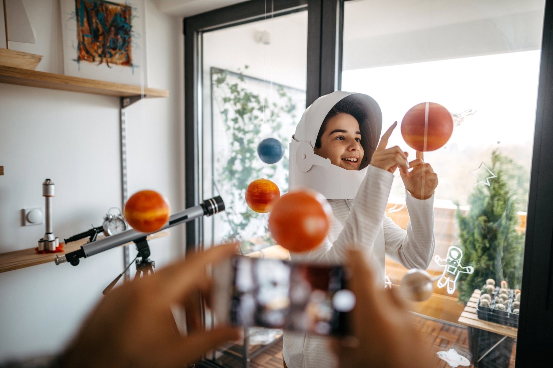A child wearing an astronaut helmet explores a model of the solar system at home, representing Golden Futures Awards that encourage creativity, learning, and future goals.