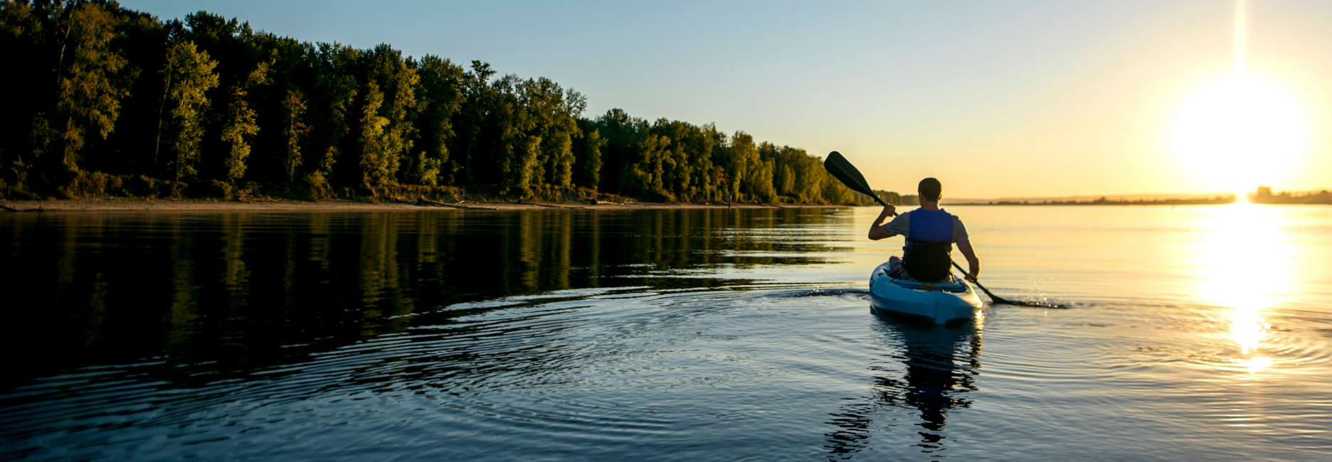 Man paddling a kayak at sunset on a river