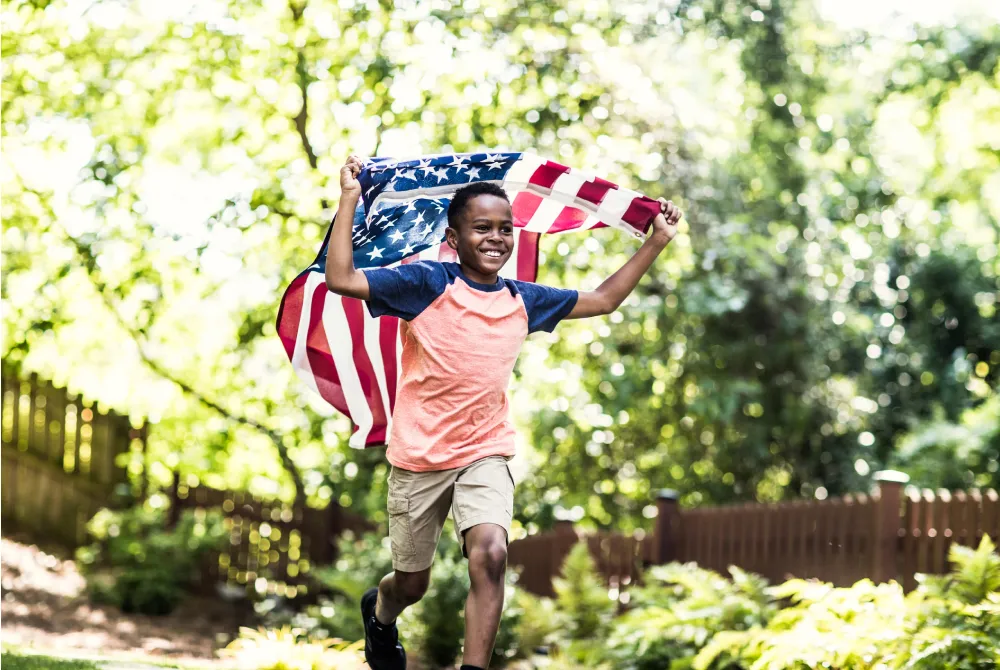 Young boy running in a park with an American Flag