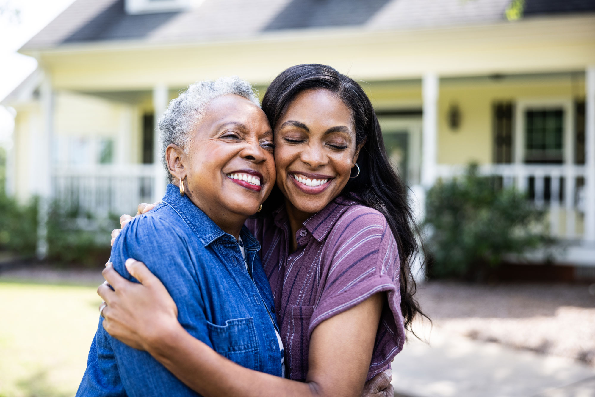 Adult daughter embracing an older woman outside a home.