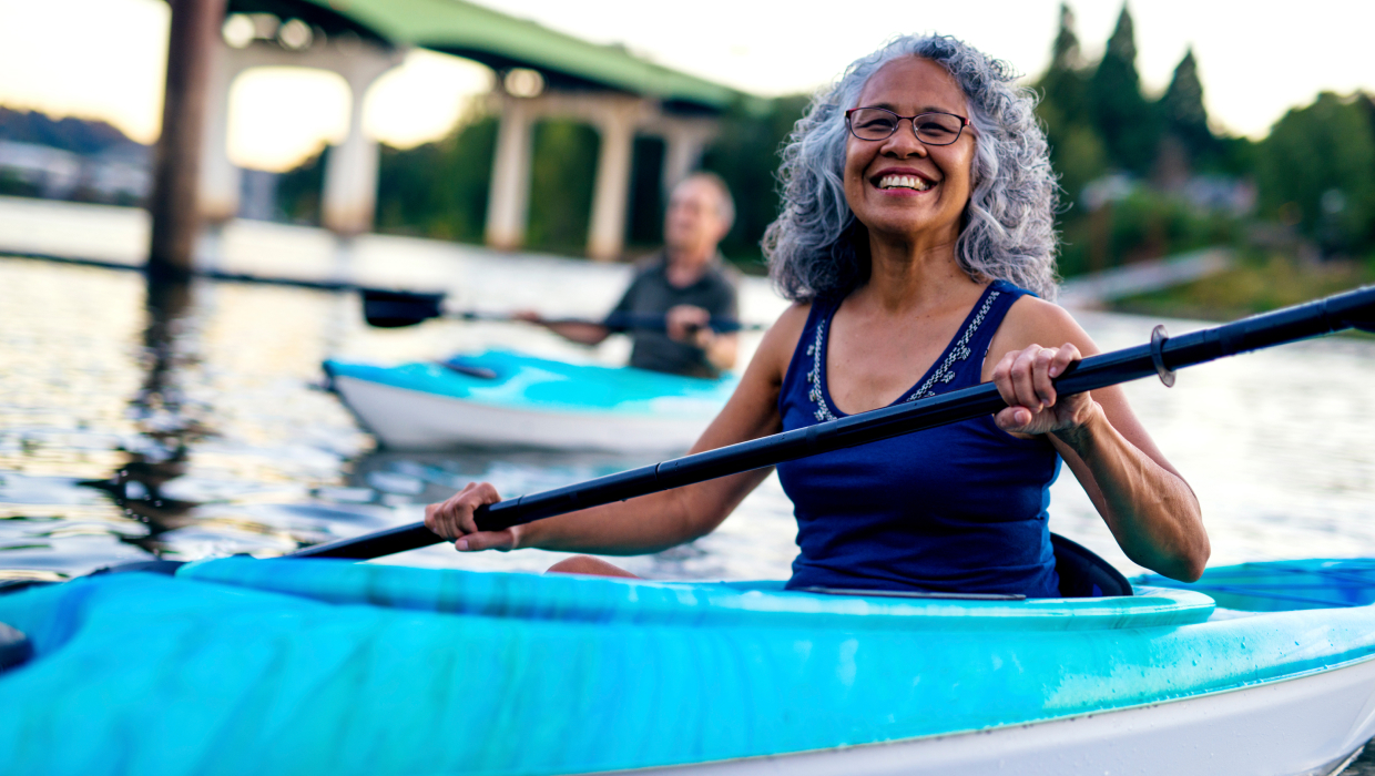 mature woman kayaking on a river with man in the background