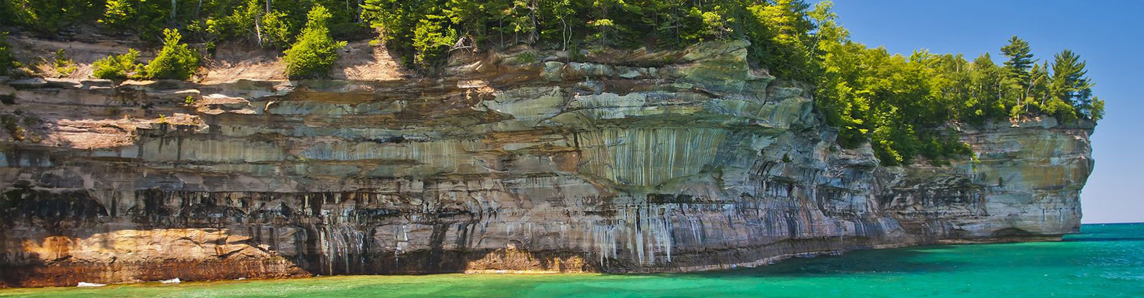 stony cliff face with trees on top above teal waters