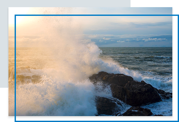 A wave crashing against the rocks at the coastline, with dynamic splashes under a cloudy sky.
