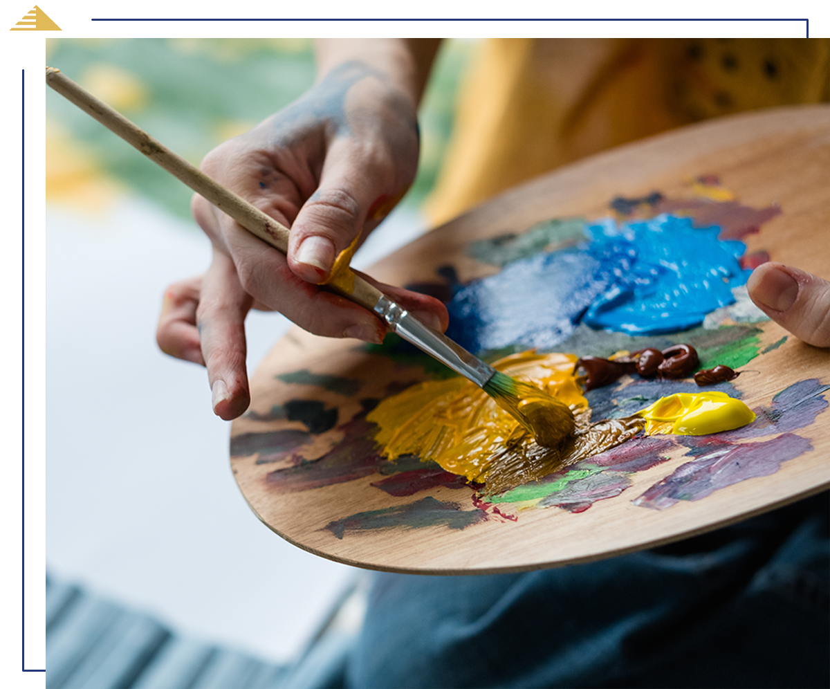 Close-up of an artist mixing yellow and brown paint on a wooden palette with a paintbrush.