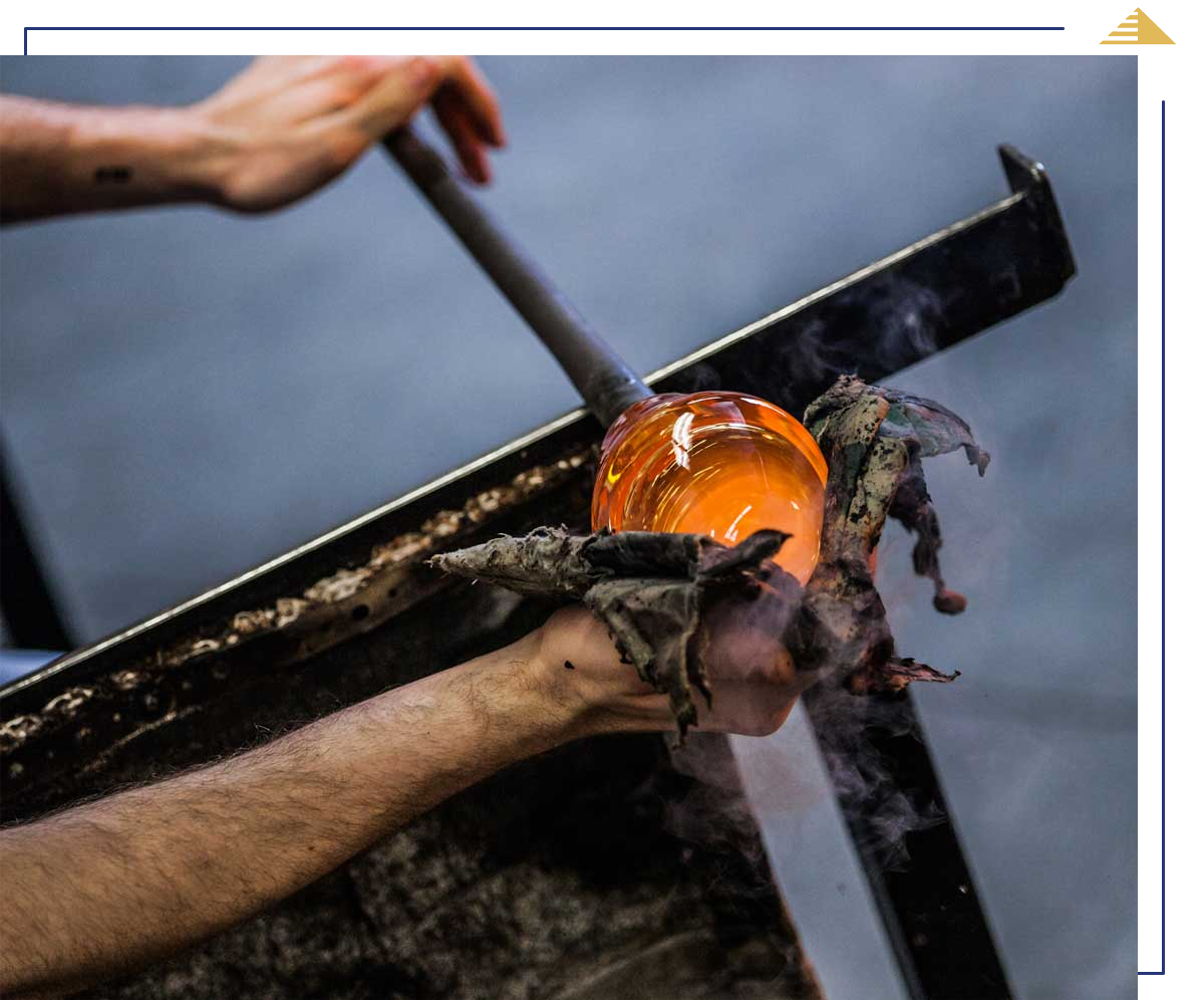Glassblower shaping molten glass with wet newspaper and a blowpipe.