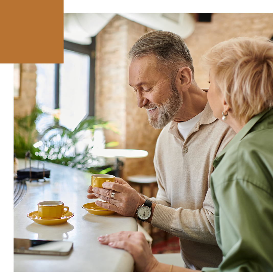 Smiling older couple sharing coffee at a cafe counter.