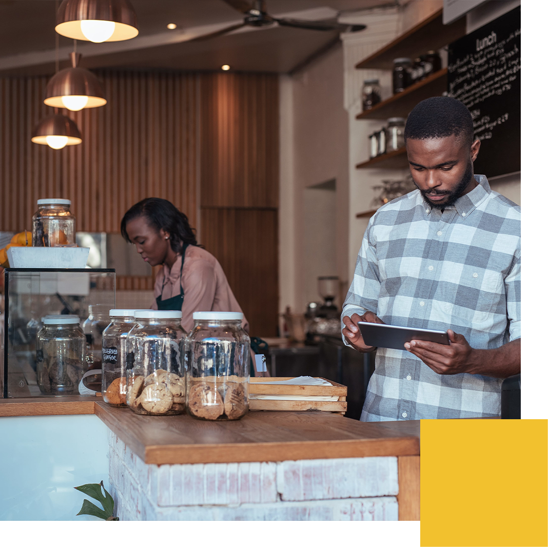 Cafe employee using a tablet at the counter while an employee works at the espresso machine behind him.