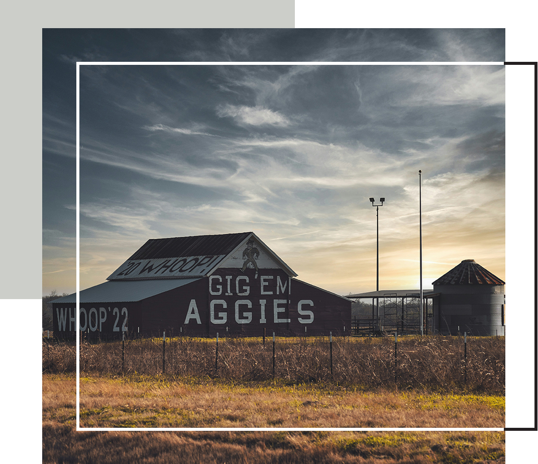 A rustic barn painted with “Gig ’Em Aggies” and “Whoop ’22” stands beneath a dramatic Texas sky at sunset