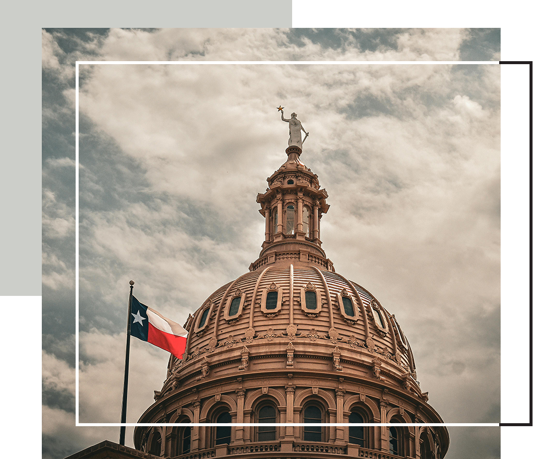The Texas State Capitol dome rises against a cloudy sky, with the Texas flag waving beside it