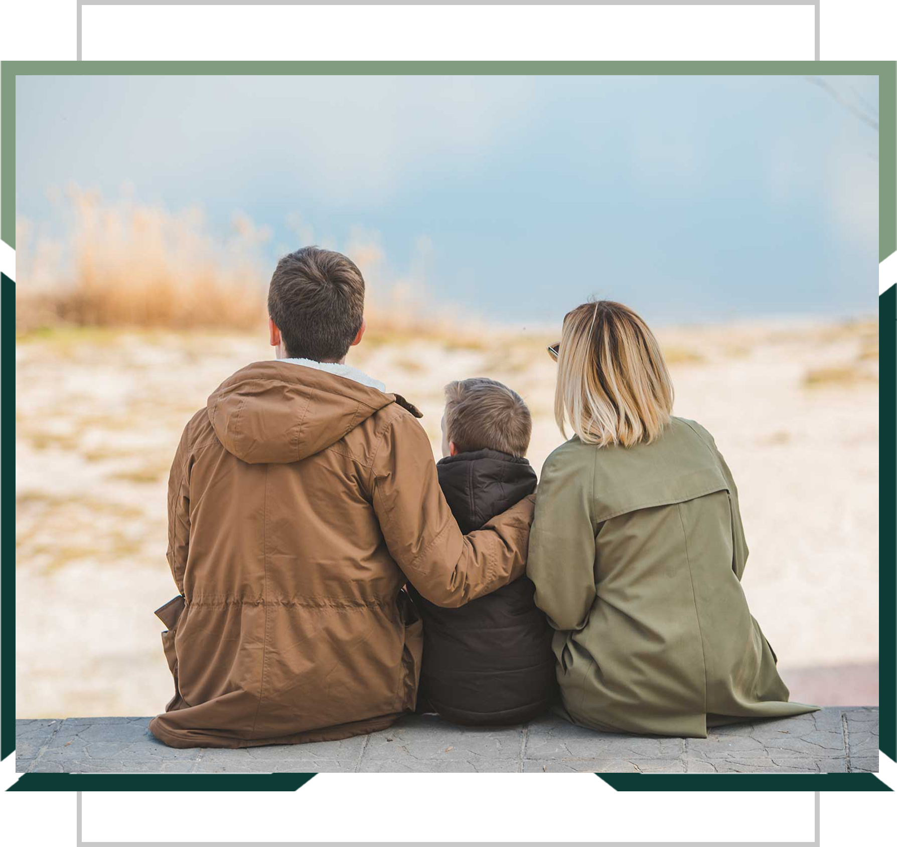 A man, child, and woman sitting close together from behind, looking out over a sandy landscape.