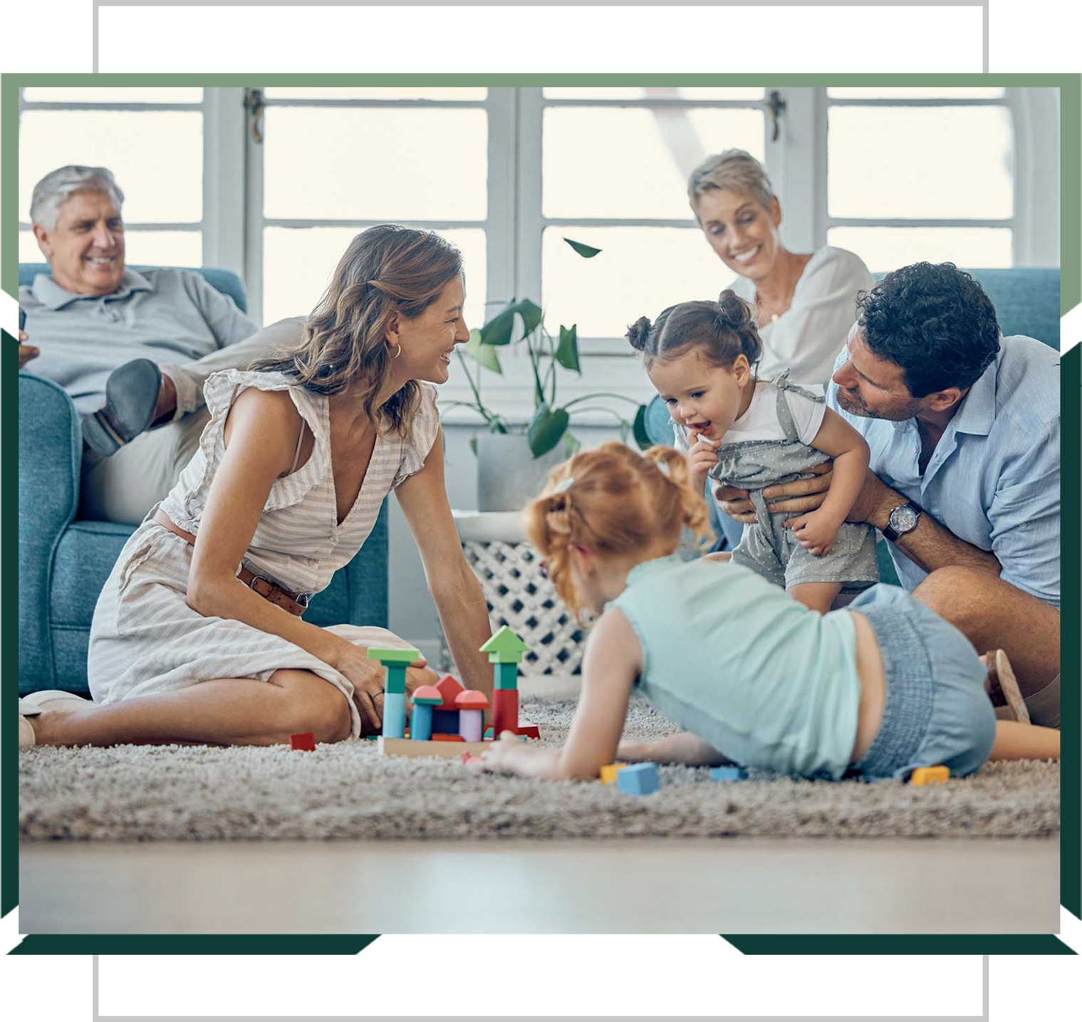 A family with three adults and three young children playing with building blocks on a living room floor.