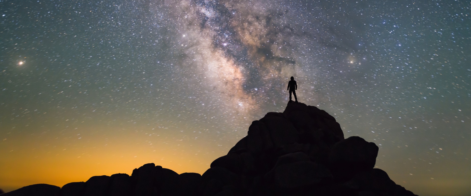 Silhouette of man on rocks against a brilliant night sky