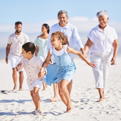 little-girl-and-boy-holding-hands-while-running-together-on-sandy-beach-while-parents-and