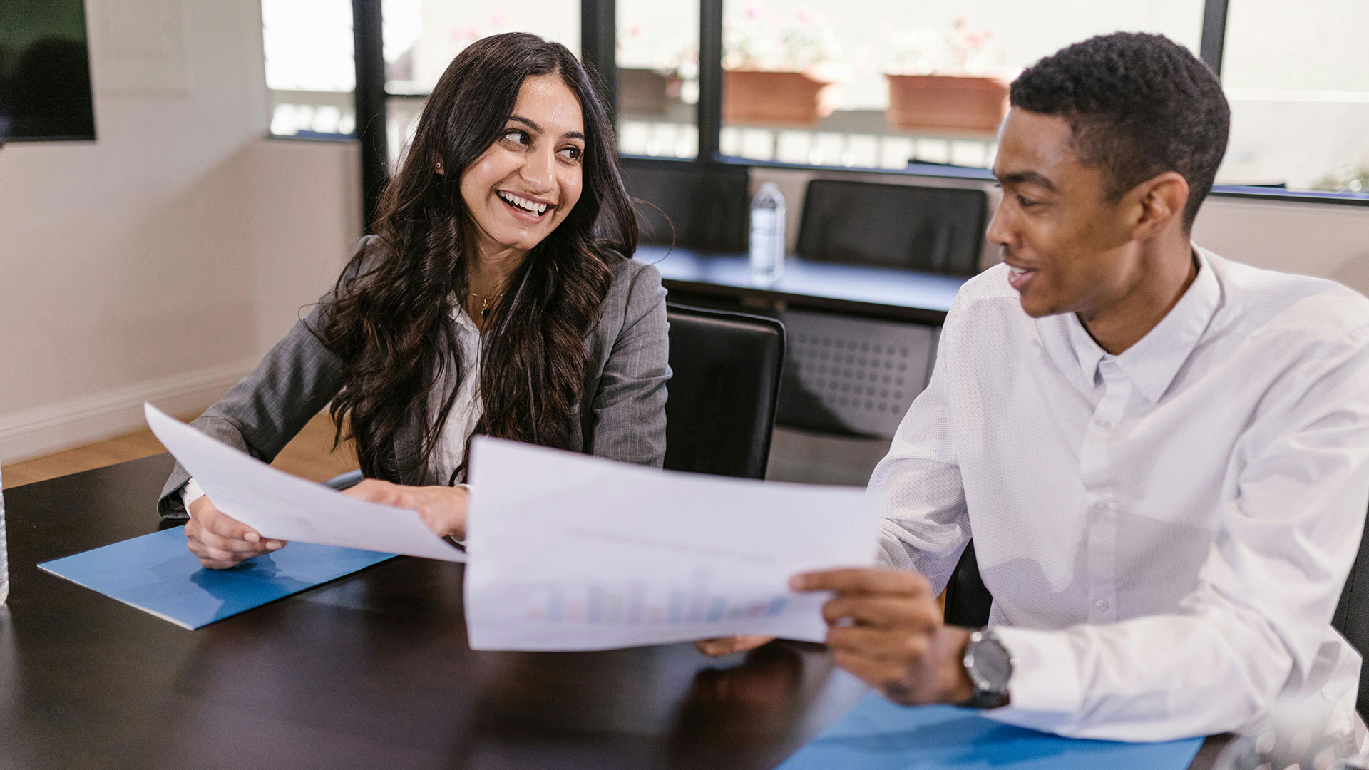 A man and a woman seated at a conference table reviewing documents and charts.