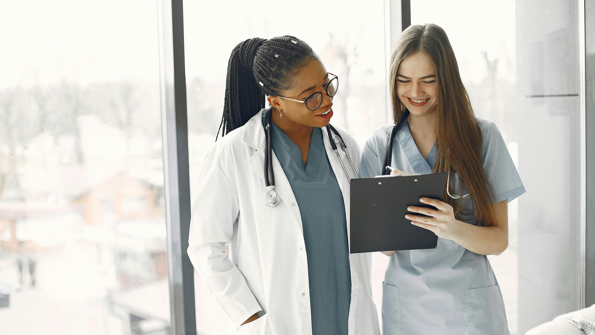Two medical professionals reviewing notes on a clipboard near a window.