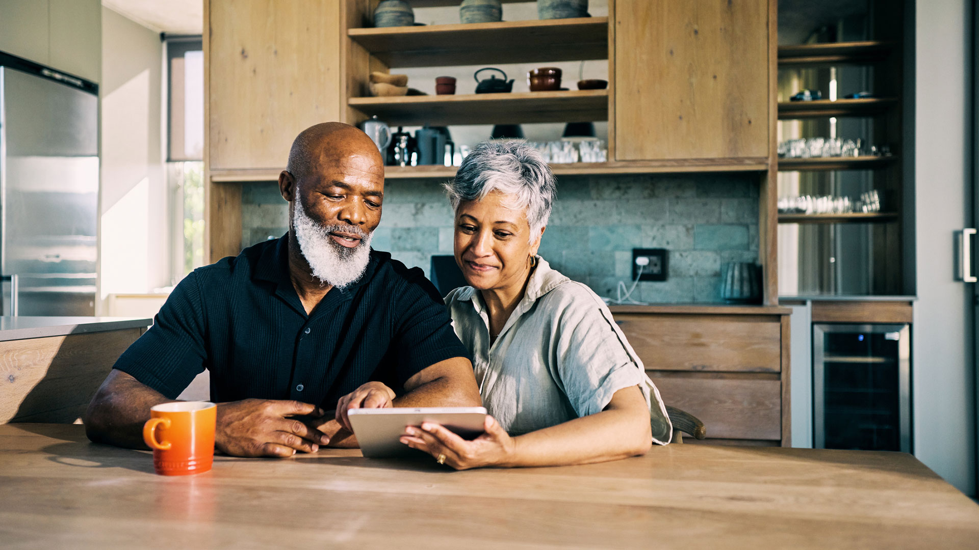 An older couple looking at a tablet together at a kitchen table.