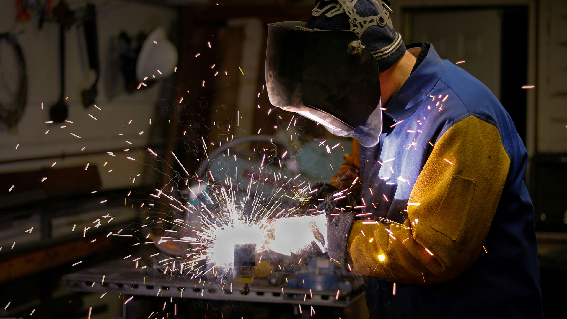 A welder in protective gear working on metal with sparks flying.
