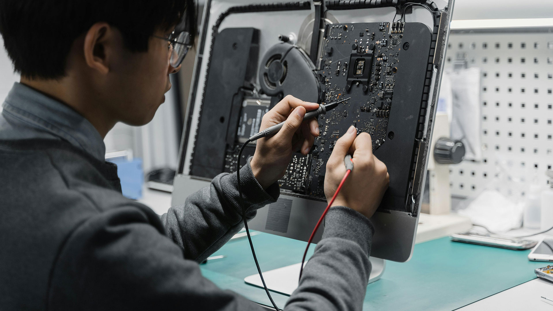 A person using a multimeter to test the internal components of a disassembled computer.