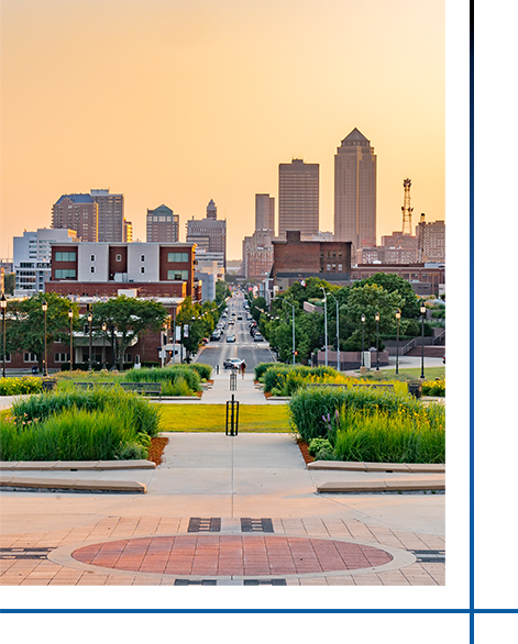 City skyline viewed from a landscaped park with a central walkway at sunset.