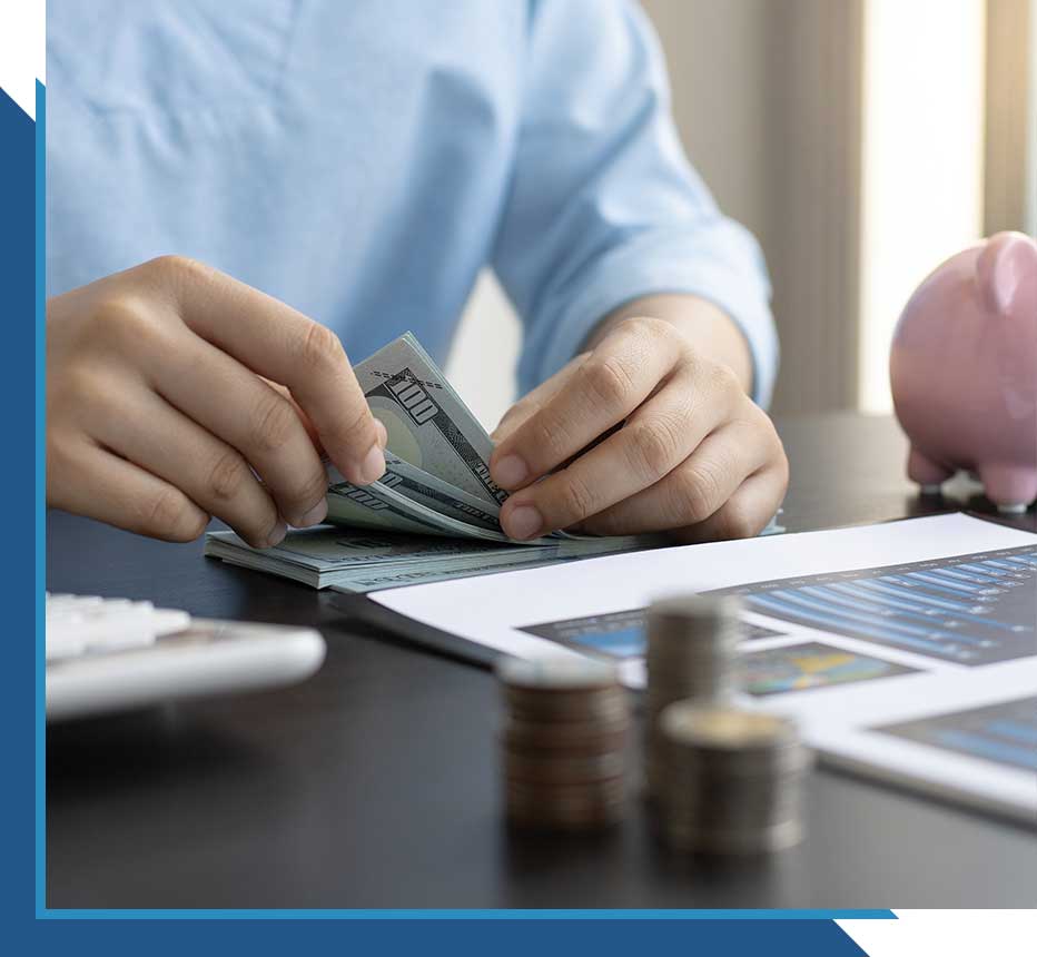 Counting cash next to financial reports and a piggy bank on a desk.