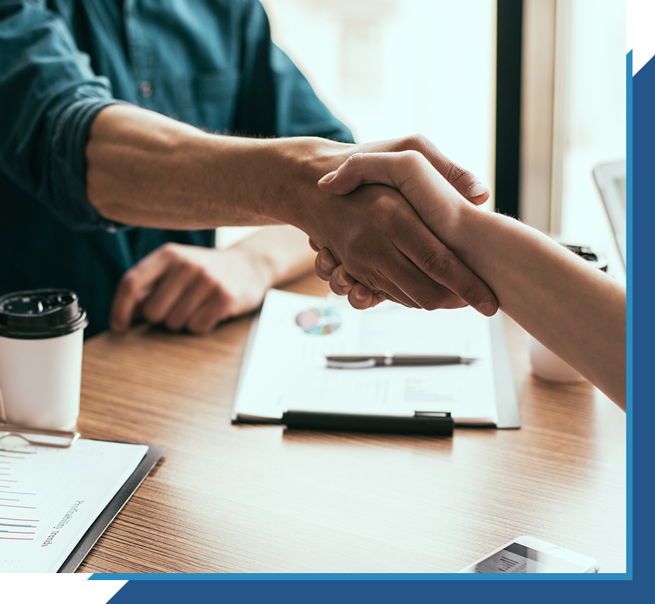 Two people shaking hands over a desk with documents, symbolizing agreement or partnership.