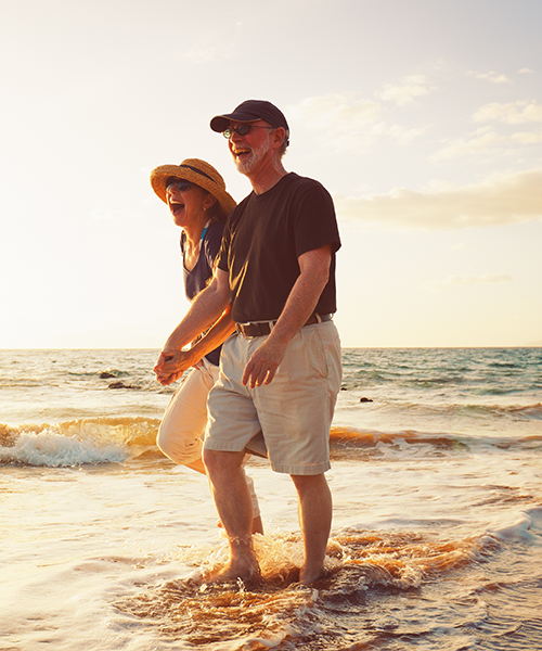 laughing couple holding hands walking in ocean surf at sunset