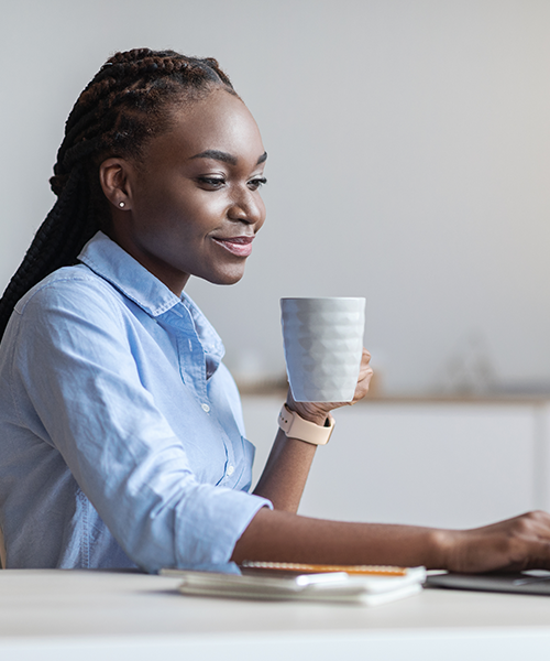 Woman holding coffee cup working at laptop