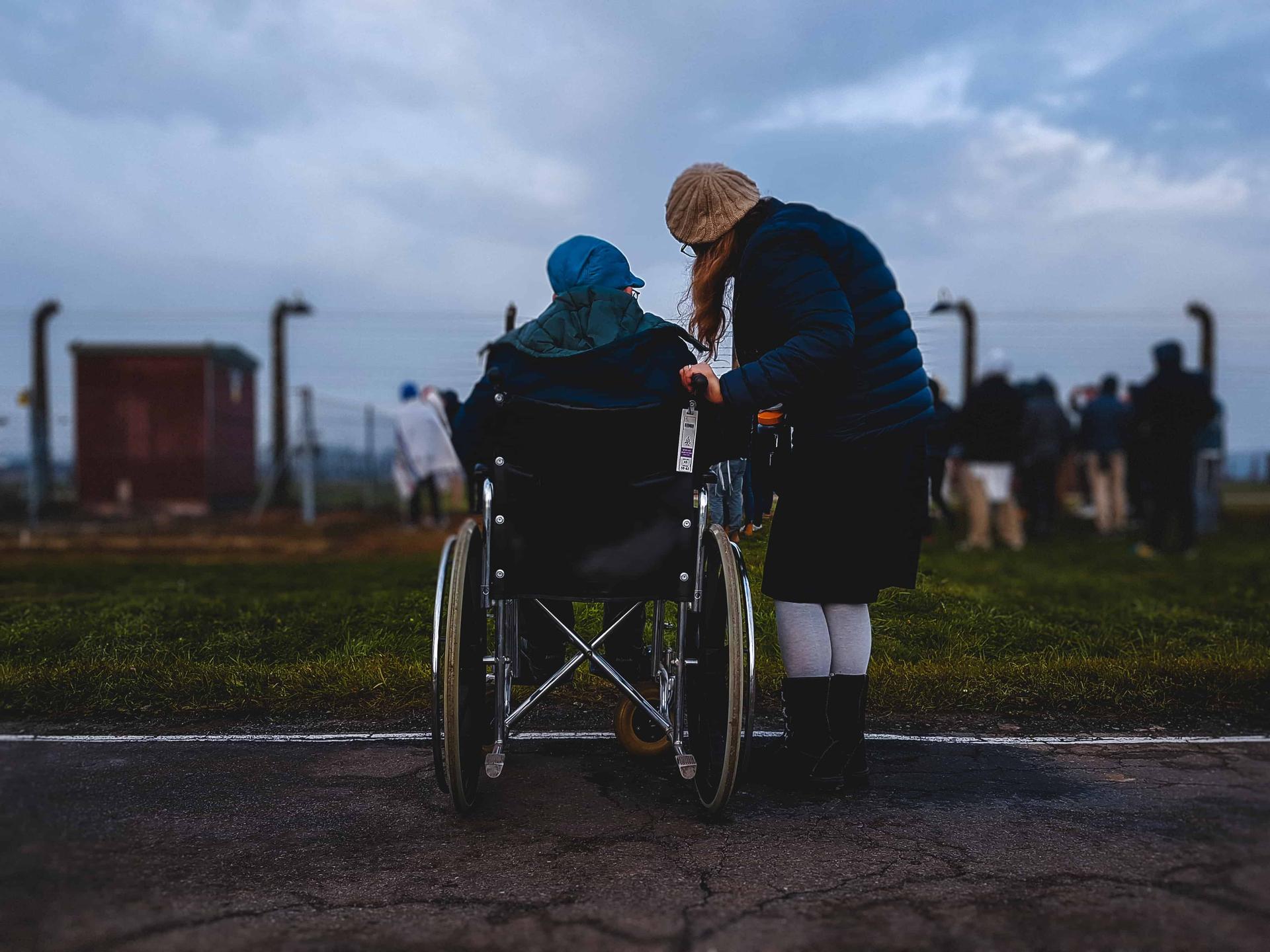View From Behind of Woman Standing Beside a Person in Wheelchair Image