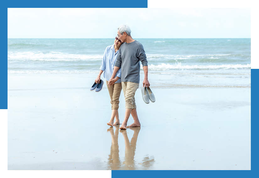 Older couple walking barefoot along the shoreline, holding hands and carrying their shoes.