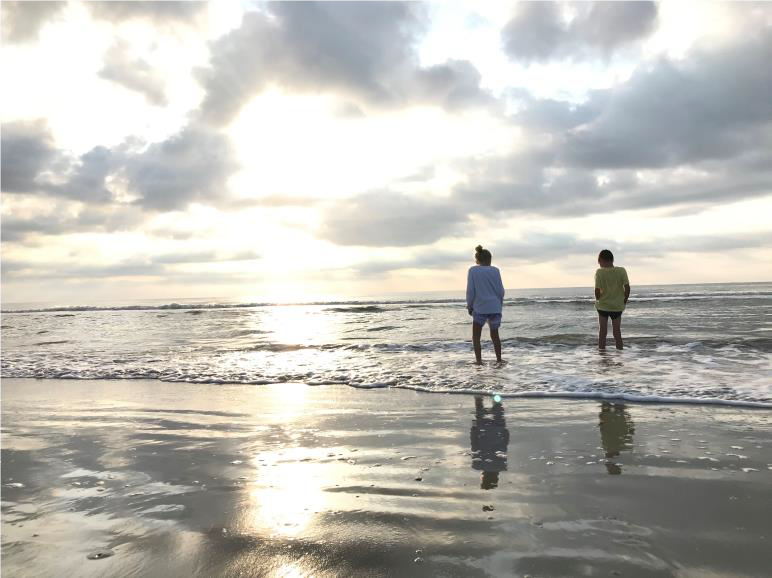 couple walking in ocean surf at beach sun and clouds in sky