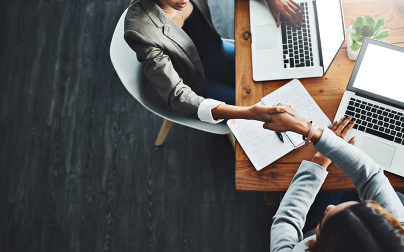 arial view of 2 women shaking hands at table with laptops