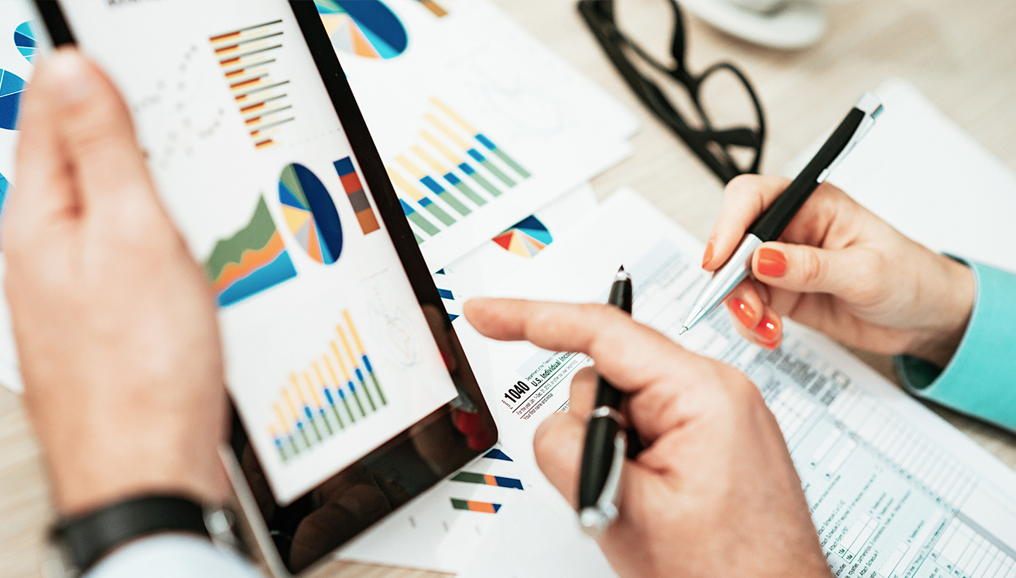 close up of 2 people with pens reviewing paper reports and tablet with data charts