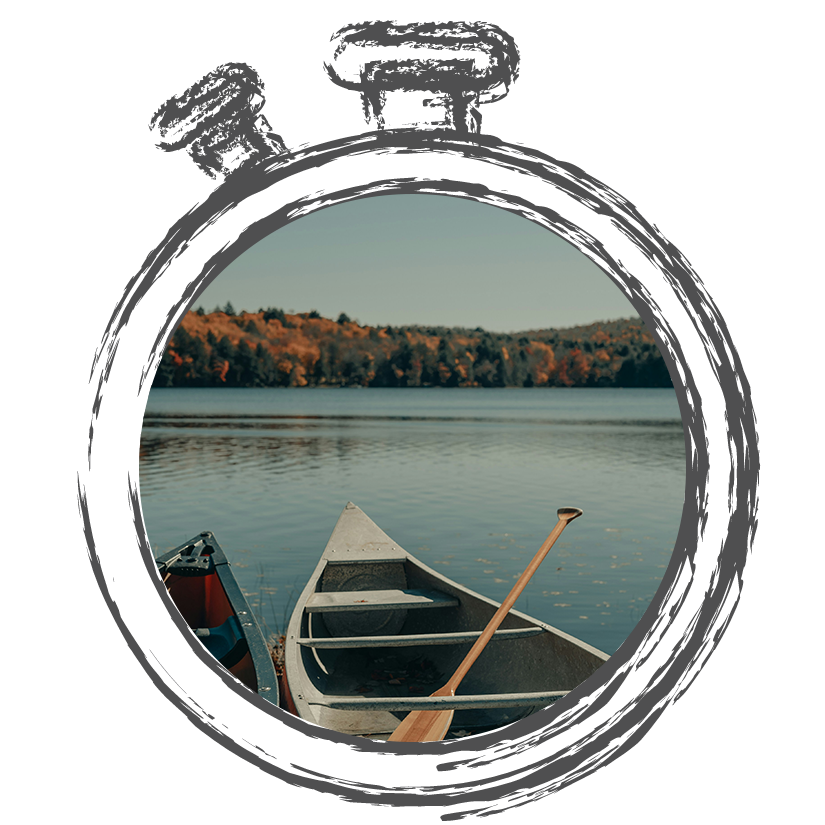 Two canoes resting by a calm lake with an autumnal backdrop and a paddle in one of the boats.