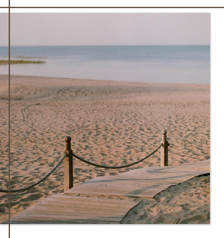 Wooden pathway leading to the beach at sunset, with soft sand and tranquil waters ahead.