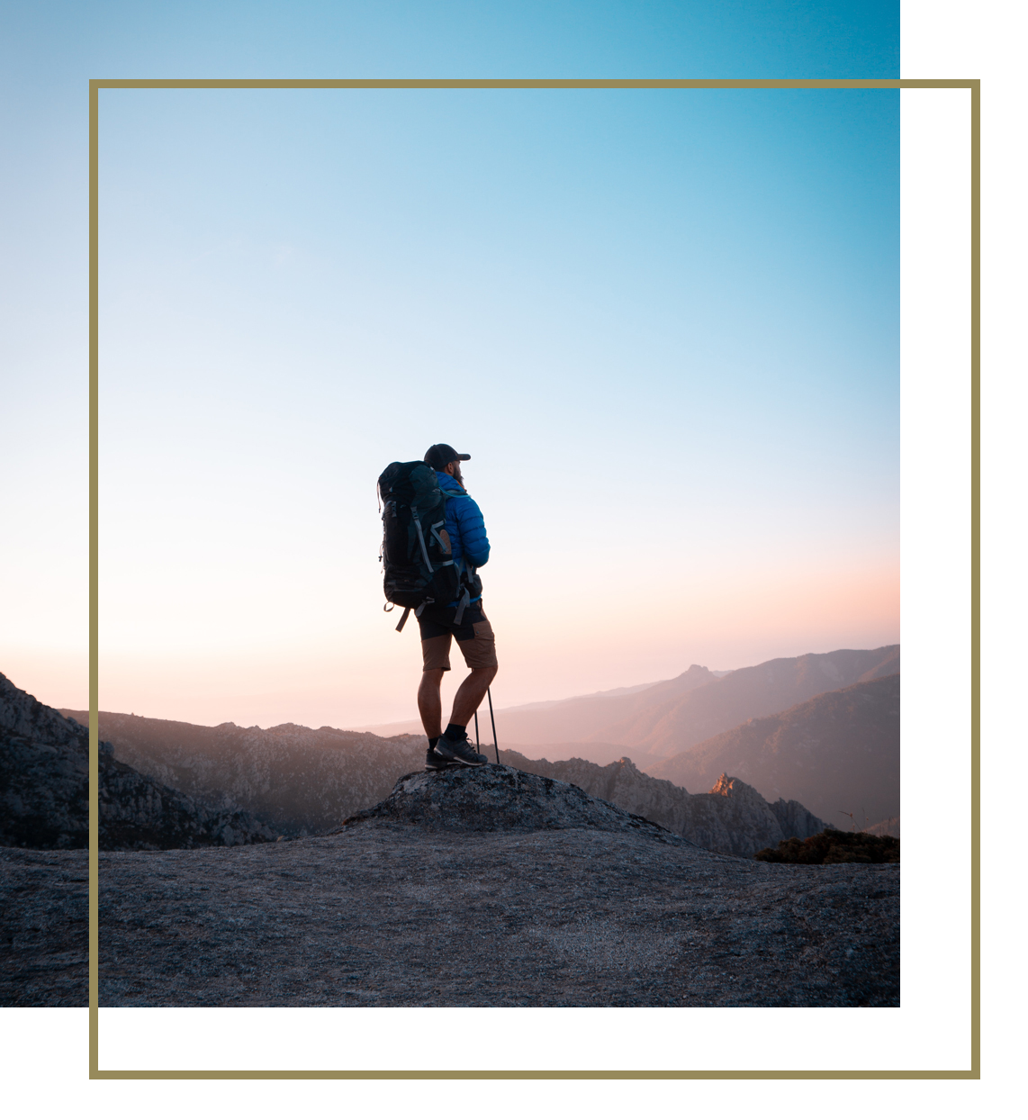 Hiker standing on a rocky peak at sunrise, taking in the panoramic mountain view.