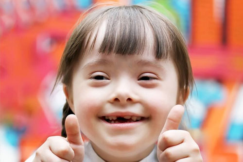 Special Needs Planning > Beautiful Downs Syndrome Girl smiling at the camera with thumbs up