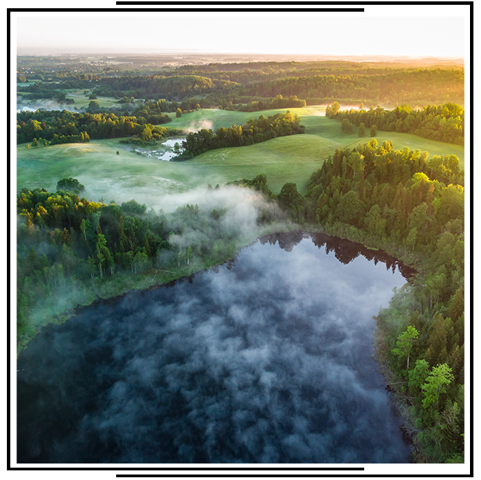 Aerial view of a misty lake nestled among vibrant green hills and dense forest at sunrise.