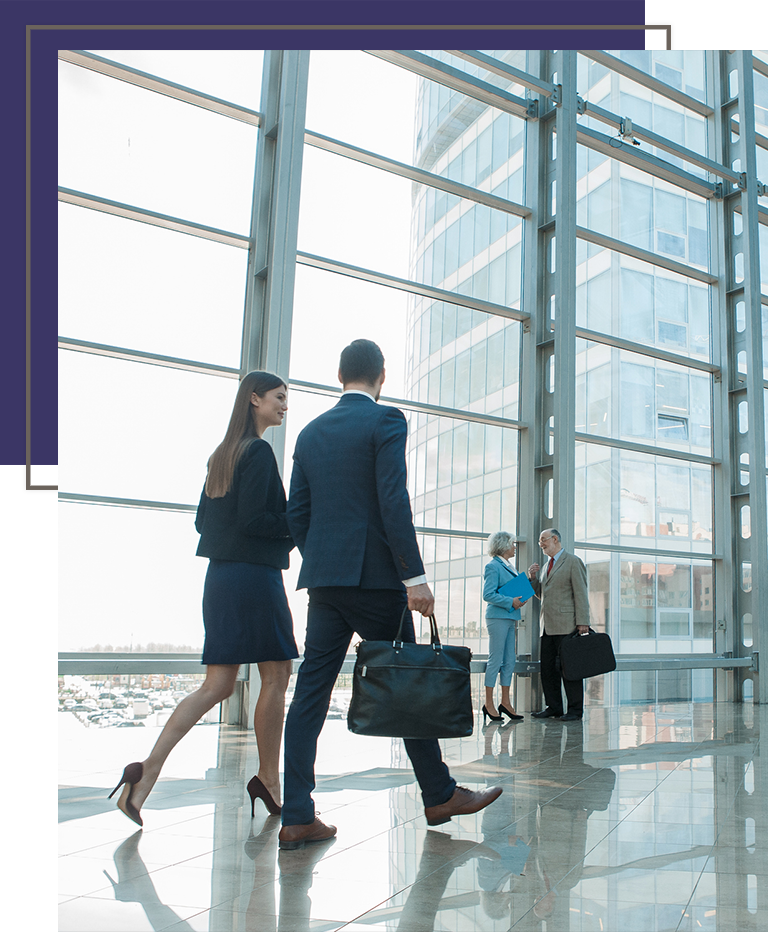 Professionals walking through a sleek, sunlit office atrium with floor-to-ceiling windows and a city view.