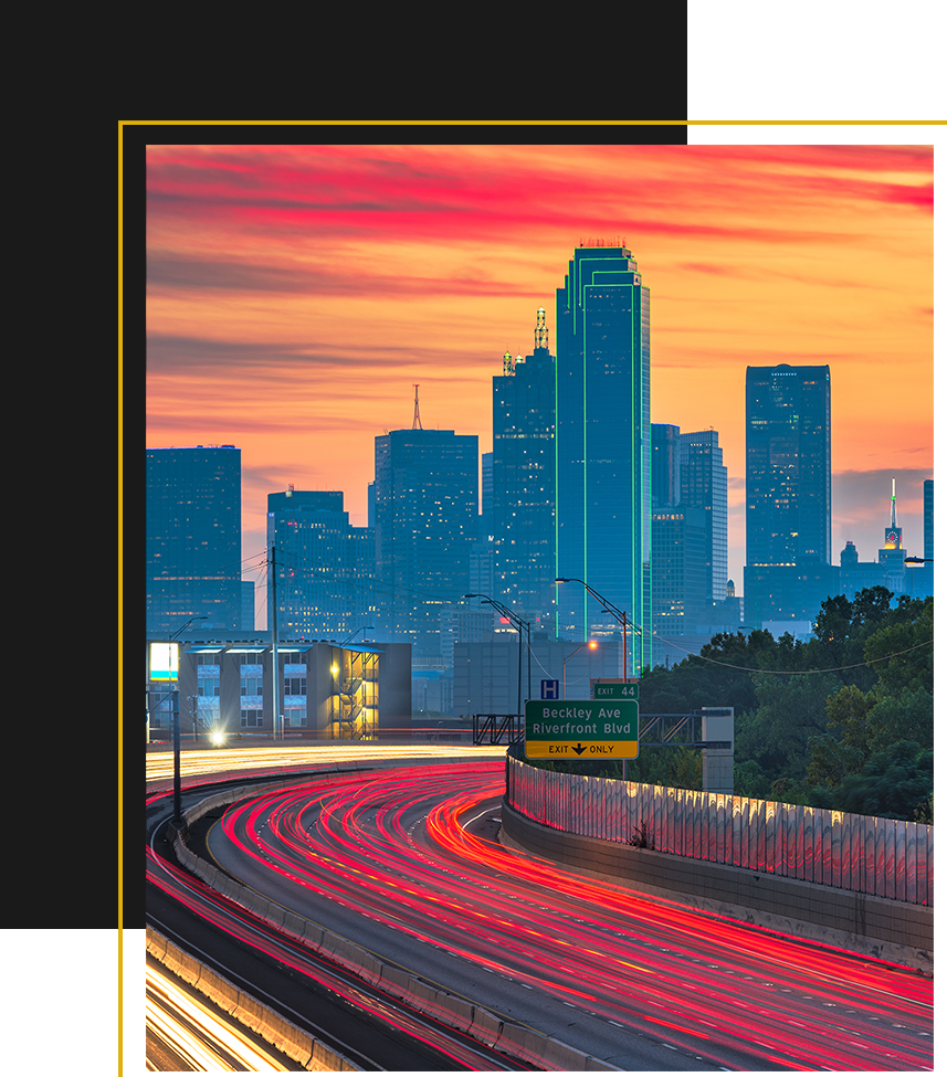 A vibrant city skyline glows at sunset as car lights streak along a busy highway