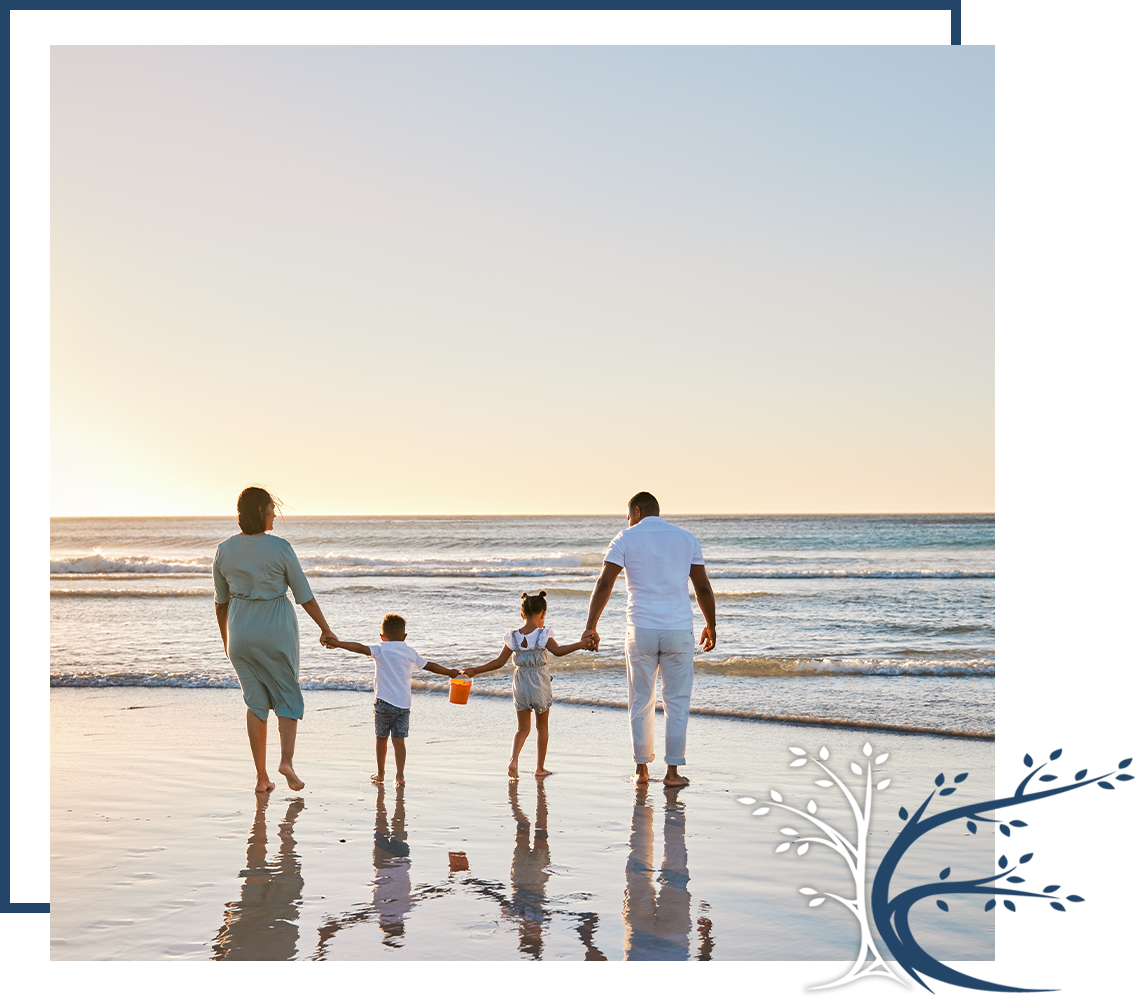 Family holding hands while walking along the shoreline at sunset with gentle waves in the background.