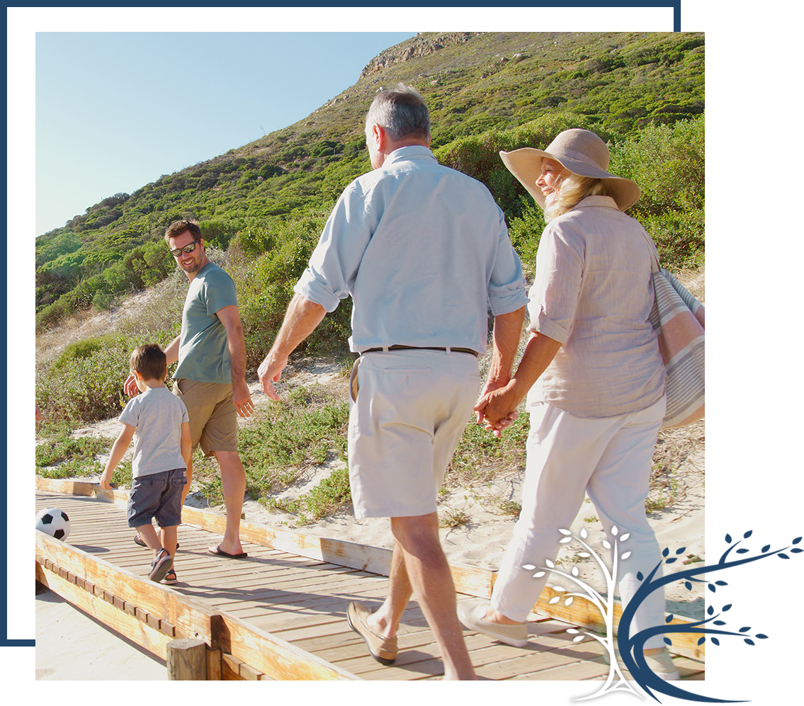 Three generations of a family walking together along a wooden boardwalk near the beach.
