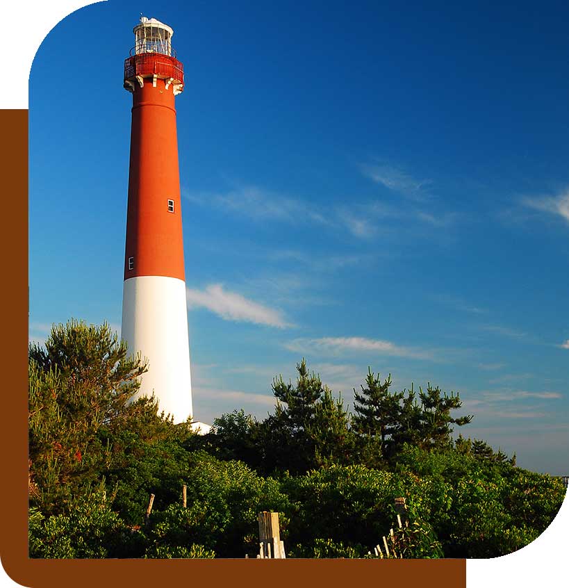 A tall lighthouse stands against a clear blue sky, surrounded by green trees.